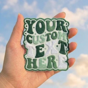 Könnte beinhalten: Ein rechteckiger bestickter Aufnäher mit gewelltem Rand, der den Text YOUR CUSTOM TEXT HERE in einer wellenförmigen Retro-Schrift zeigt. Das Design verwendet eine Farbpalette aus dunkelwaldgrünem, salbeigrünem und weißem Garn auf hellem Stoff.