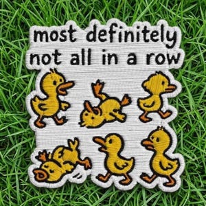 May include: An embroidered patch with a white background and black text that reads most definitely not all in a row. The patch features six yellow ducklings in various poses, including some walking, one lying on its back, and one tumbling.