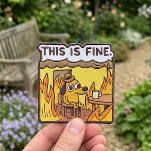 Puede incluir: Un parche bordado rectangular que muestra un perro de dibujos animados con sombrero, sentado a una mesa con una taza en una habitación llena de llamas naranjas y amarillas. El texto THIS IS FINE. está impreso en letras negras sobre fondo blanco.