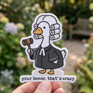 May include: An embroidered patch featuring a white goose dressed as a judge in a black robe and white wig, holding a brown wooden gavel. Below the goose, a white banner contains the black text, "your honor. that's crazy" in lowercase letters.