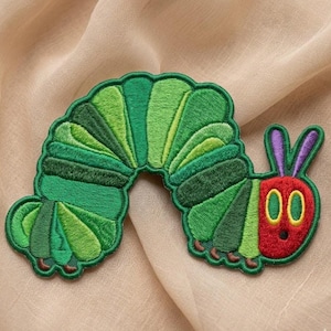May include: An embroidered patch shaped like a caterpillar with a red head, purple antennae, and a segmented body featuring various shades of green. The design includes yellow eyes with green pupils and small brown feet along the bottom edge.