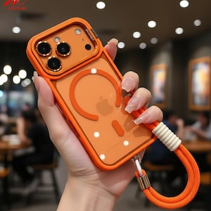 May include: Orange phone case with a matching lanyard. The case has a clear back with an orange border and a circular design. The lanyard is orange with a white accent.