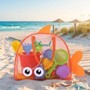 Puede incluir: Una bolsa de playa de malla naranja con forma de pez, con aleta dorsal y cola. La bolsa tiene grandes ojos blancos, asas naranjas y el nombre Shanel impreso en color verde azulado. Está llena de juguetes de arena de plástico de colores.