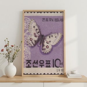 Op de afbeelding: Een ingelijste verticale wandkunstprint met een postzegelontwerp in vintage-stijl op een lichtpaarse achtergrond. De postzegel toont een gedetailleerde witte vlinder met donkere stippen en roze accenten, Koreaanse tekst en het jaartal 1961.