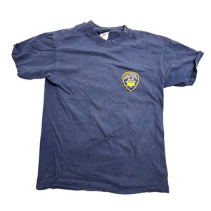 May include: Navy blue t-shirt featuring a small patch with the words "California Highway Patrol" in yellow and blue. The shirt is a crew neck style and appears to be made of a soft, worn material. The shirt is slightly wrinkled.