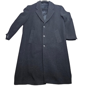 May include: A long, dark charcoal gray overcoat featuring a notched lapel, a three-button front closure, and two vertical side pockets. The coat has long sleeves with three small buttons on each cuff and a smooth, dark interior lining visible at the collar.