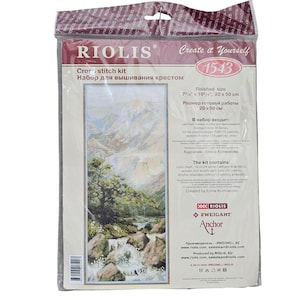 May include: A Riolis cross stitch kit 1543 in a clear plastic package. The kit features a mountain landscape with a waterfall and pine trees. The finished size is 7 3/4 inches by 19 3/4 inches. The packaging includes text and brand logos.