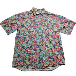 May include: A short-sleeved shirt with a colourful floral design. The shirt has a navy blue base, covered in red, green, and turquoise flowers and leaves. The collar and button-up front are clearly visible.