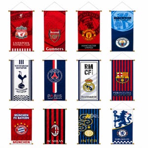 Pode incluir: Uma coleção de doze estandartes de parede retangulares de tecido com vários logotipos e nomes de clubes de futebol profissionais, incluindo Liverpool, Arsenal, Manchester United, Manchester City, Tottenham, Paris Saint-Germain, Real Madrid, Barcelona, Bayern Munique, AC Milan, Inter de Milão e Chelsea.