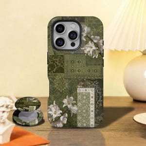 Puede incluir: Funda de teléfono verde con diseño de patchwork y detalles de flores blancas. La funda presenta una variedad de patrones y texturas, incluyendo diseños florales y geométricos. También se ve un soporte para teléfono a juego.