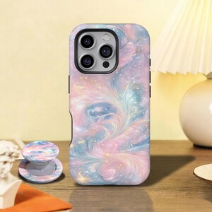 May include: A smartphone case and a matching circular collapsible phone grip featuring a swirling, ethereal pattern of pastel pink, blue, and lavender hues with subtle gold glitter accents. The case has a black camera lens cutout.