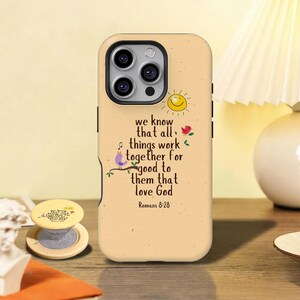 May include: A tan phone case featuring a scripture quote, a smiling sun, and a bird on a branch. The text reads "we know that all things work together for good to them that love God Romans 8:28". A matching phone grip is also visible.