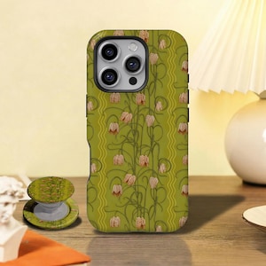 May include: A green phone case with a floral pattern featuring brown and pink flowers and green stems. A matching phone grip is next to the phone case. The phone case is on a wooden surface.