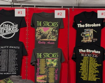 Peut inclure: Une collection de t-shirts à manches courtes noirs et gris anthracite arborant la marque du groupe The Strokes. Les t-shirts présentent divers motifs graphiques, dont une illustration de camion et les dates de la tournée The World 2026, avec le texte Reality Awaits.