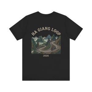 Pode incluir: T-shirt preto com um gráfico de uma estrada de montanha e o texto "HA GIANG LOOP" e o ano "2026". O design usa tons de verde, castanho e bege.