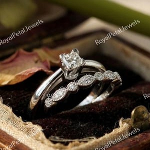 May include: A two-piece engagement ring set in a wooden box. The set includes a solitaire ring with a square-cut diamond and a band with multiple small, round diamonds. The rings are set against a dark brown velvet lining.