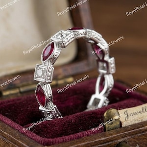 Può includere: Una fede in argento con rubini rossi taglio marquise e diamanti bianchi taglio quadrato alternati. La fascia in metallo presenta intricati dettagli milgrain e motivi incisi lungo i lati, creando un aspetto strutturato.