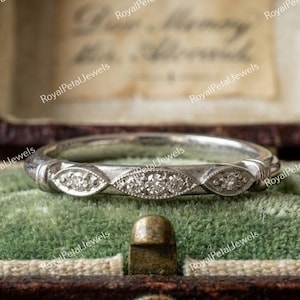 May include: A silver-toned metal band ring featuring three marquise-shaped settings, each containing small clear stones. The ring has a textured, milgrain-style edge along the decorative front section, showcasing a detailed, vintage-inspired design.