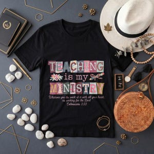 May include: A black short-sleeved t-shirt featuring the colorful text "TEACHING is my MINISTRY" with floral accents and a pencil graphic, followed by the scripture "Whatever you do, work at it with all your heart, as working for the Lord Colossians 3:23".