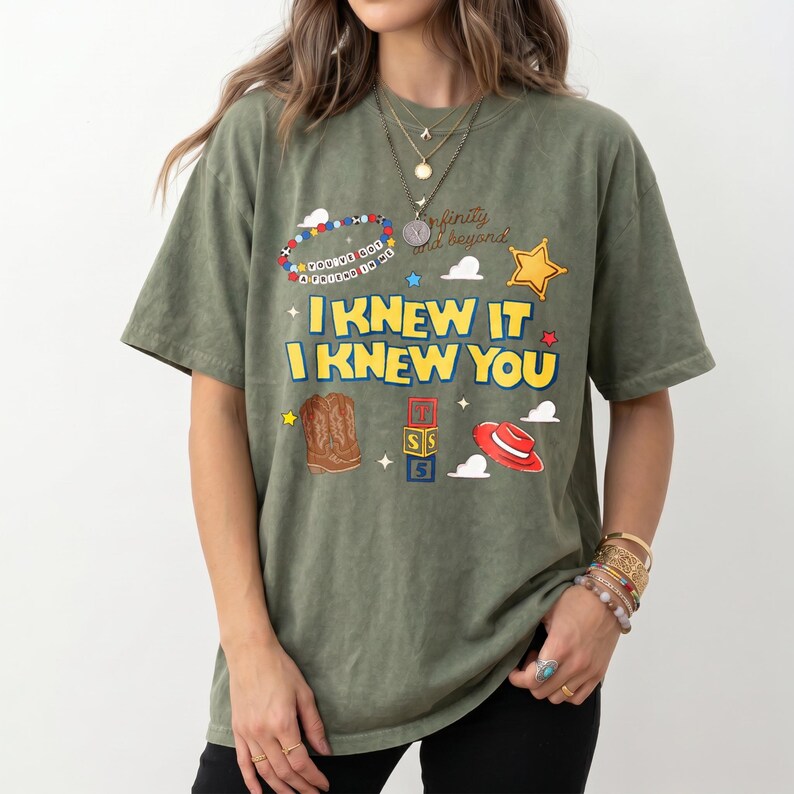 Puede incluir: Una camiseta de manga corta color verde oliva con un estampado gr&aacute;fico que incluye el texto I KNEW IT I KNEW YOU, una estrella de sheriff, botas vaqueras, bloques de letras, un sombrero rojo y un dise&ntilde;o de pulsera de cuentas con el texto YOU'VE GOT A FRIEND IN ME.