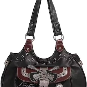 Puede incluir: Bolso de mano negro con herrajes plateados y diseño de guitarra. El bolso presenta un bolsillo burdeos con tachuelas plateadas y cierre de hebilla. Las asas son negras con costuras blancas y aros plateados.