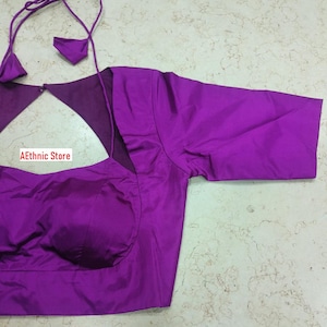 May include: A striking purple blouse with a keyhole back and short sleeves. The blouse has a tailored fit and is made of a smooth, shiny fabric. The text "AEthnic Store" is visible in the lower left corner.