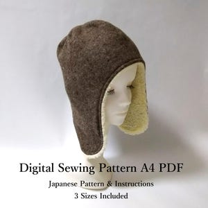 以下が含まれることがあります： マネキンの頭に展示された、クリーム色のフェイクファーの裏地が付いた、茶色の冬用帽子。耳あて付き。帽子はデジタル縫製パターンで、日本語の説明書と3つのサイズが含まれています。