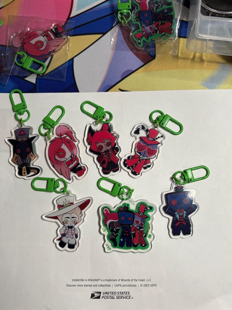 May include: A collection of eight acrylic keychains featuring stylized cartoon characters with button eyes, each attached to a bright green plastic lobster clasp. The characters are depicted in various outfits and colors, including red, white, and black.