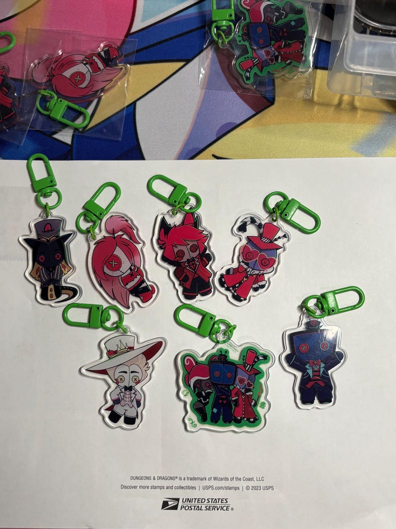 May include: A collection of seven clear acrylic keychains featuring various cartoon character designs with vibrant pink, red, black, and white color schemes. Each keychain is attached to a bright green plastic lobster clasp hook for easy attachment.