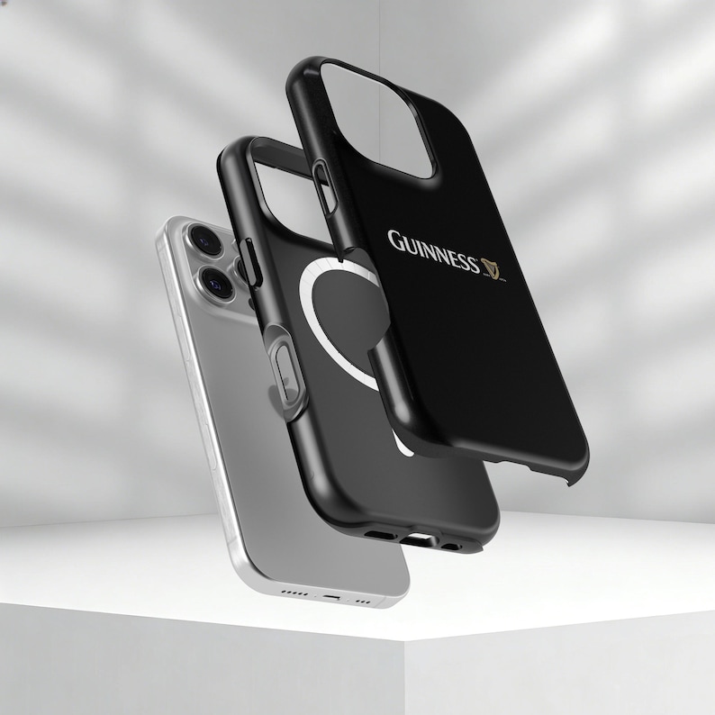 May include: Three black iPhone cases with the Guinness logo and a silver iPhone. The cases are black with a white circular design and the Guinness logo in gold. The phone is silver.