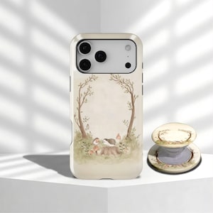 Op de afbeelding: Een crèmekleurige telefoonhoes en bijpassende popsocket met een grillige bosscène met een egel, paddenstoelen en bomen. De hoes heeft een beschermende bumper en een glanzende afwerking. De popsocket is rond en heeft een inklapbaar ontwerp.