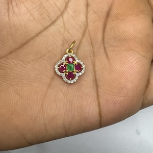 May include: A gold pendant with a four-leaf clover design. Each leaf features a round, red gemstone, with a square, green gemstone at the center. The clover is outlined with small, clear gemstones.