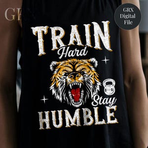May include: Black tank top with a distressed white and yellow graphic. The graphic features a roaring bear with the words "TRAIN Hard STAY HUMBLE" in a bold, vintage font. A kettlebell icon is also included.