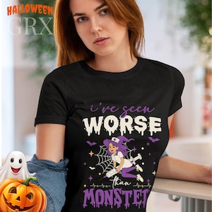 Può includere: Una t-shirt nera con la grafica di un'infermiera con capelli viola e cappello da strega, che tiene in mano una grande siringa. Il testo recita I've seen WORSE than MONSTERS, circondato da ragnatele, piccoli pipistrelli e stelle viola, bianche e arancioni.
