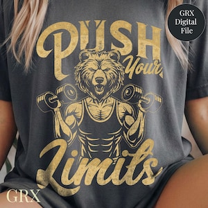 Può includere: T-shirt grigio scuro con una grafica dorata invecchiata di un orso che solleva pesi. Il testo "PUSH Your Limits" è sopra l'orso. La maglietta ha un aspetto vintage e l'orso è muscoloso e determinato.