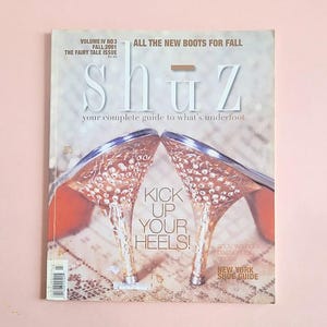 May include: A magazine cover titled "Shuz" with the text "All the New Boots for Fall" and "Kick Up Your Heels!". The cover features a pair of high-heeled shoes with clear heels and red soles. The magazine is from Fall 2001.