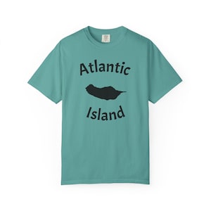 Puede incluir: Una camiseta de manga corta color verde azulado con el texto negro Atlantic Island impreso en un diseño curvo y una silueta negra con forma de isla situada entre las dos palabras en la parte frontal de la prenda.