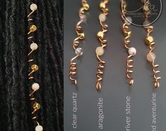 May include: Close-up of four copper hair accessories with different gemstone beads. The gemstones include clear quartz, aragonite, river stone, and red aventurine. The accessories are designed to be inserted into locs or braids.