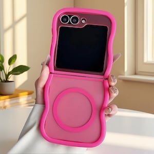 Puede incluir: Una funda de teléfono rosa brillante con un diseño único. La funda tiene un borde ondulado y un acento circular en la mitad inferior. La pantalla del teléfono es negra. La funda está diseñada para un teléfono plegable.