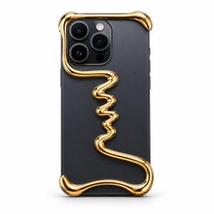 Puede incluir: Una funda de smartphone en negro mate con un marco en relieve de color oro metálico con aspecto líquido, que envuelve los bordes y forma una silueta abstracta y ondulada en la parte posterior, rodeando el módulo de triple cámara.