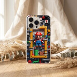 May include: Clear phone case featuring a colorful design of a Lego-style Mario figure inside a yellow and gray structure. The case has a clear border and a detailed, playful aesthetic, with a brick wall and green pipes.