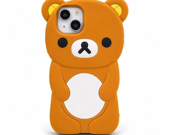 Op de afbeelding: Oranje beer-vormige telefoonhoes met zwarte ogen en een zwarte mond. De hoes heeft een witte buik en gele accenten op de oren. De camera van de telefoon is zichtbaar door de hoes.