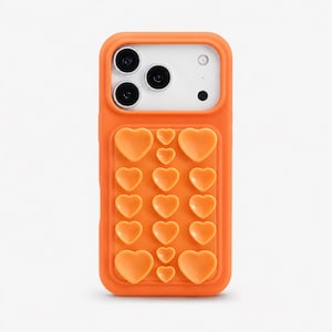Peut inclure: Coque de téléphone orange avec un motif en forme de cœur. L'étui a une forme rectangulaire avec une section en relief de formes de cœur. La zone de la caméra est blanche avec trois objectifs noirs et un petit point noir.