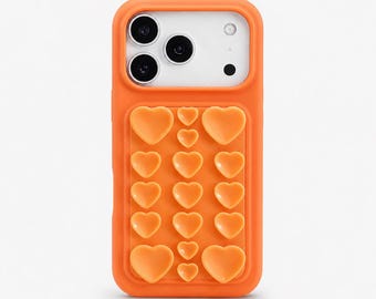 Op de afbeelding: Oranje telefoonhoesje met een hartvormig ontwerp. De hoes heeft een rechthoekige vorm met een verhoogd gedeelte van hartvormen. De camera is wit met drie zwarte cameralenzen en een kleine zwarte stip.