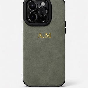 Peut inclure: Coque de téléphone vert olive avec un cadre de caméra noir. Le boîtier présente les initiales dorées "A.M." centrées au dos. Le boîtier a un aspect texturé semblable à du daim.