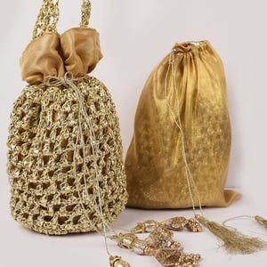 Könnte beinhalten: Zwei goldfarbene Kordelzugbeutel. Die Tasche links hat ein gewebtes, offenes Design mit einem satinartigen Oberteil und Griffen. Die Tasche rechts ist goldfarben. Dekorative Quasten mit goldenen Perlen und Fransen sind im Vordergrund.