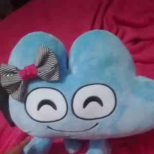 May include: A light blue plush toy in the shape of the number four, featuring large white eyes and a smiling mouth. It has small arms and legs, and a black and white striped bow with a pink centre. The toy is on a pink surface.