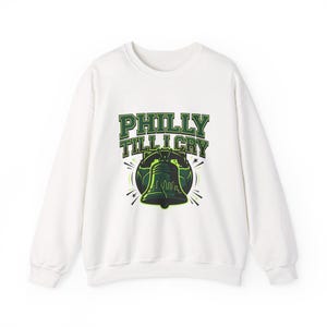 Könnte beinhalten: Weißes Sweatshirt mit dem Text "PHILLY TILL I CRY" in grünen Blockbuchstaben. Das Design beinhaltet eine grüne Liberty Bell-Grafik mit einer Stadtbild-Silhouette. Ein lässiges, bequemes Oberteil.