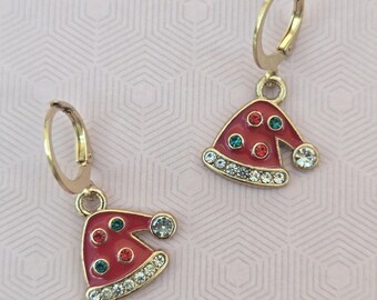 May include: A pair of gold-tone hoop earrings featuring dangling Santa hat charms. The hats are finished in red enamel with small embedded red and green rhinestones, and a row of clear rhinestones along the brim and on the pom-pom tip.