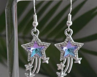 May include: Silver star earrings with a large, multi-colored star pendant. The star has a purple and blue center, surrounded by clear crystals. Three smaller stars dangle below the main star, creating a celestial design.